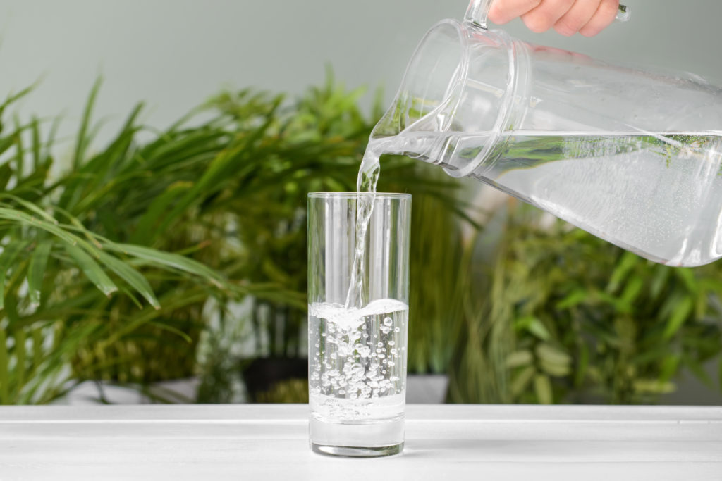 Pouring of fresh water into glass on table