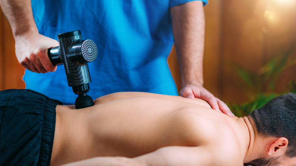 Massage Gun Treatment. Physical Therapist Massaging Man’s Lower Back