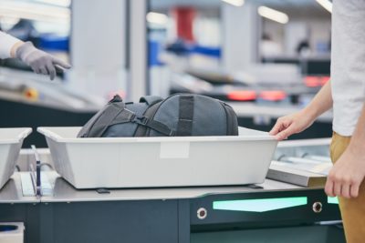 man putting a backpack in airport security scanner tray