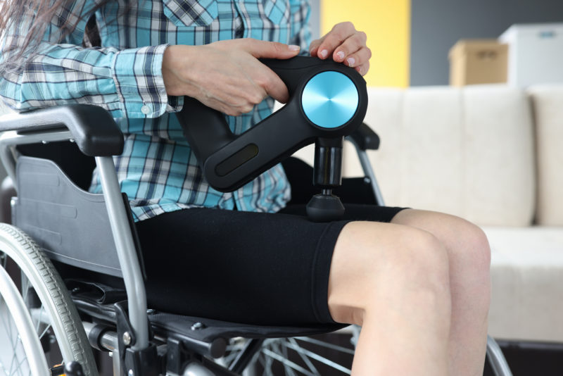 woman using a massage gun on her in a wheelchair