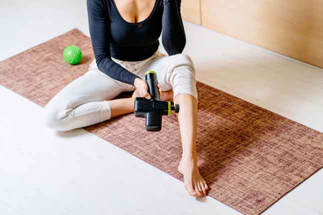 woman using massage gun on leg during workout